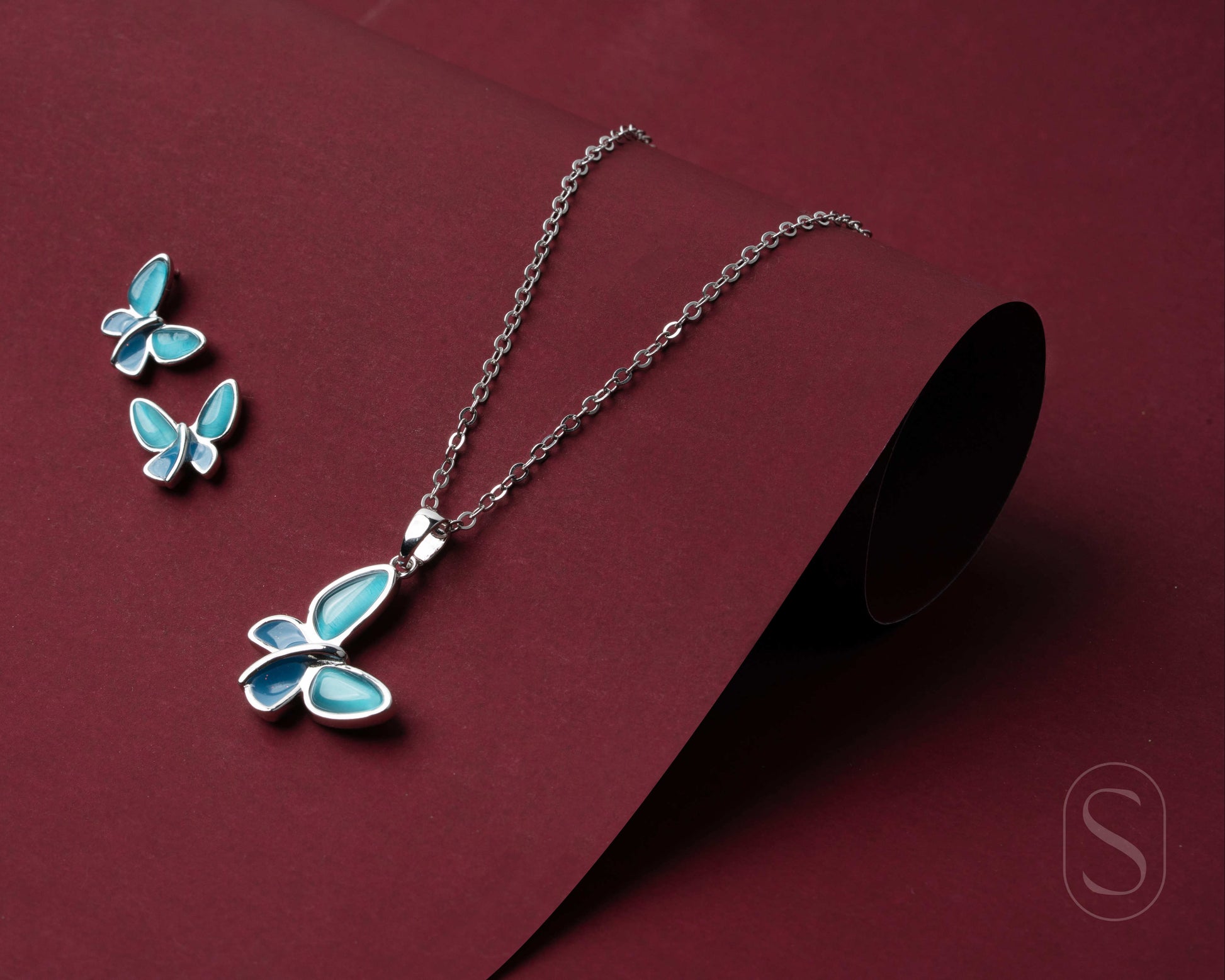 Butterfly necklace and earrings on a maroon background